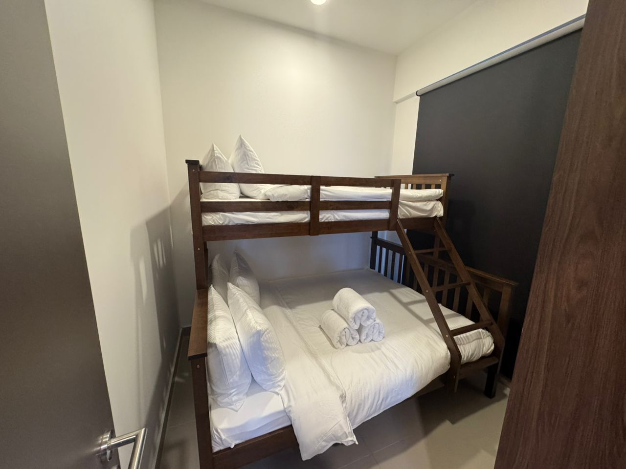 A bunk bed with white bedding and pillows, a wooden headboard, and a small wooden chair.