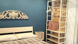 A bedroom with a bed, a white headboard, a decorative wall piece, a wardrobe with patterned curtains, and a small bedside table. - Double room with private bathroom "Chez Nous" (La Spezia)