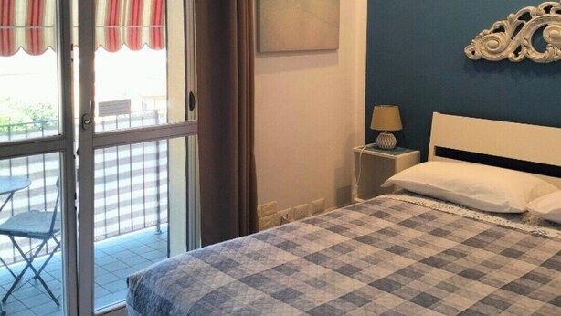 A bedroom with a bed, a nightstand, a wall-mounted artwork, and a view through a sliding glass door to an outdoor area with a striped awning. - Double room with private bathroom "Chez Nous" (La Spezia)