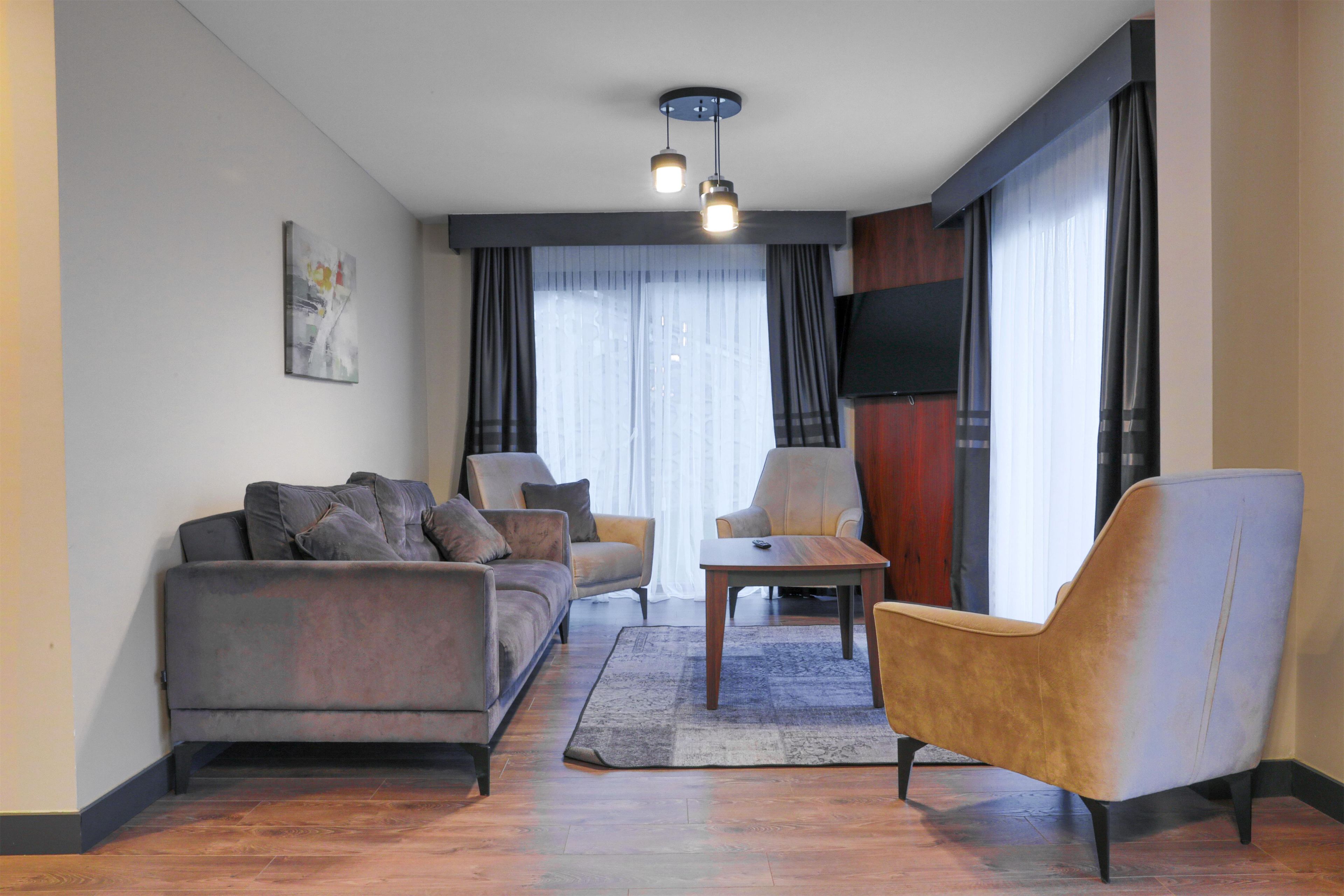 Una sala de estar moderna con sofá, sillón y mesa de centro, un televisor de pantalla plana montado en la pared y un amplio ventanal con cortinas.