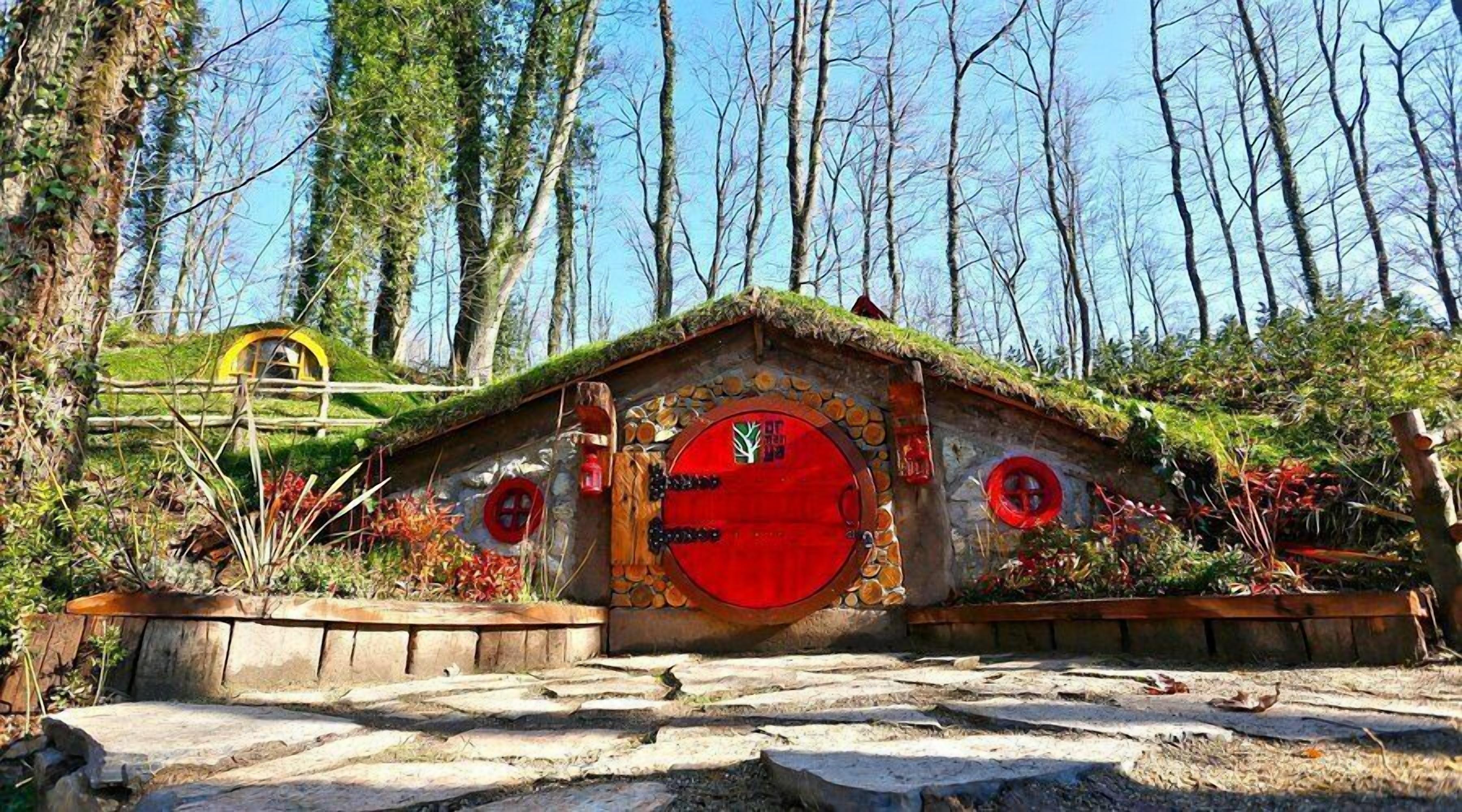 A rustic cabin with a stone facade, a red door, and a thatched roof.