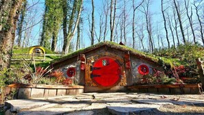 Une cabane rustique avec une façade en pierre, une porte rouge et un toit de chaume.