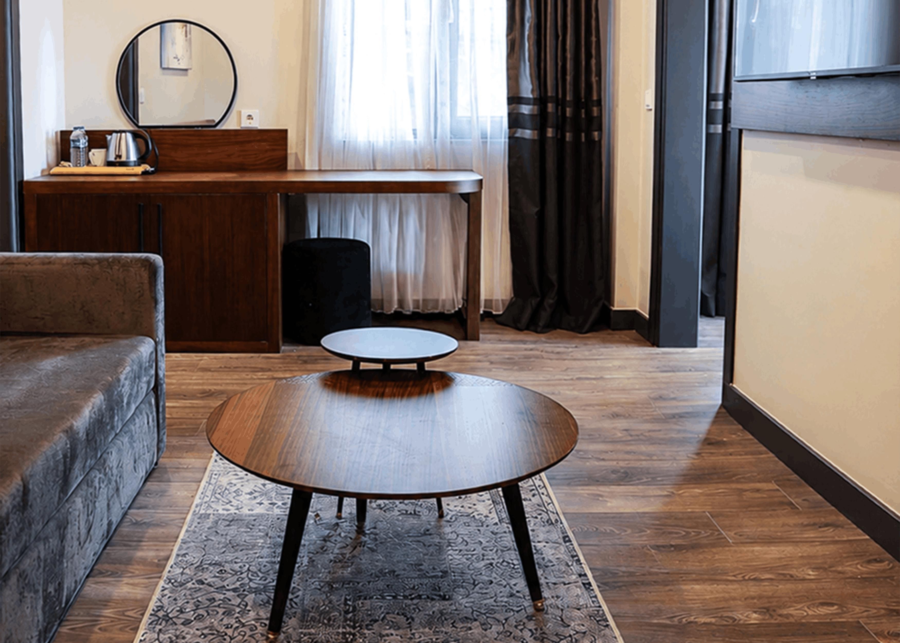 Una sala de estar con una mesa redonda, un sofá, un escritorio con espejo y una ventana con cortinas.