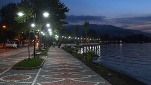 Une promenade au bord d’un lac, éclairée par des lampadaires, avec un véhicule garé à proximité.