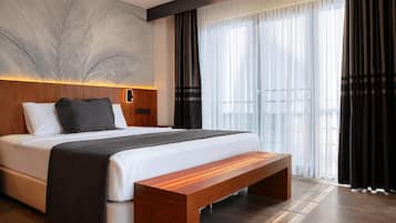 Een moderne hotelkamer met een groot bed, een houten bankje, een wandlamp en een groot raam met gordijnen.