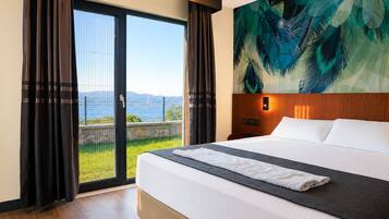 A hotel room with a large bed, a view of the sea through a glass door, and a tropical-themed wall mural.