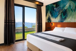 A hotel room with a large bed, a view of the sea through a glass door, and a tropical-themed wall mural.