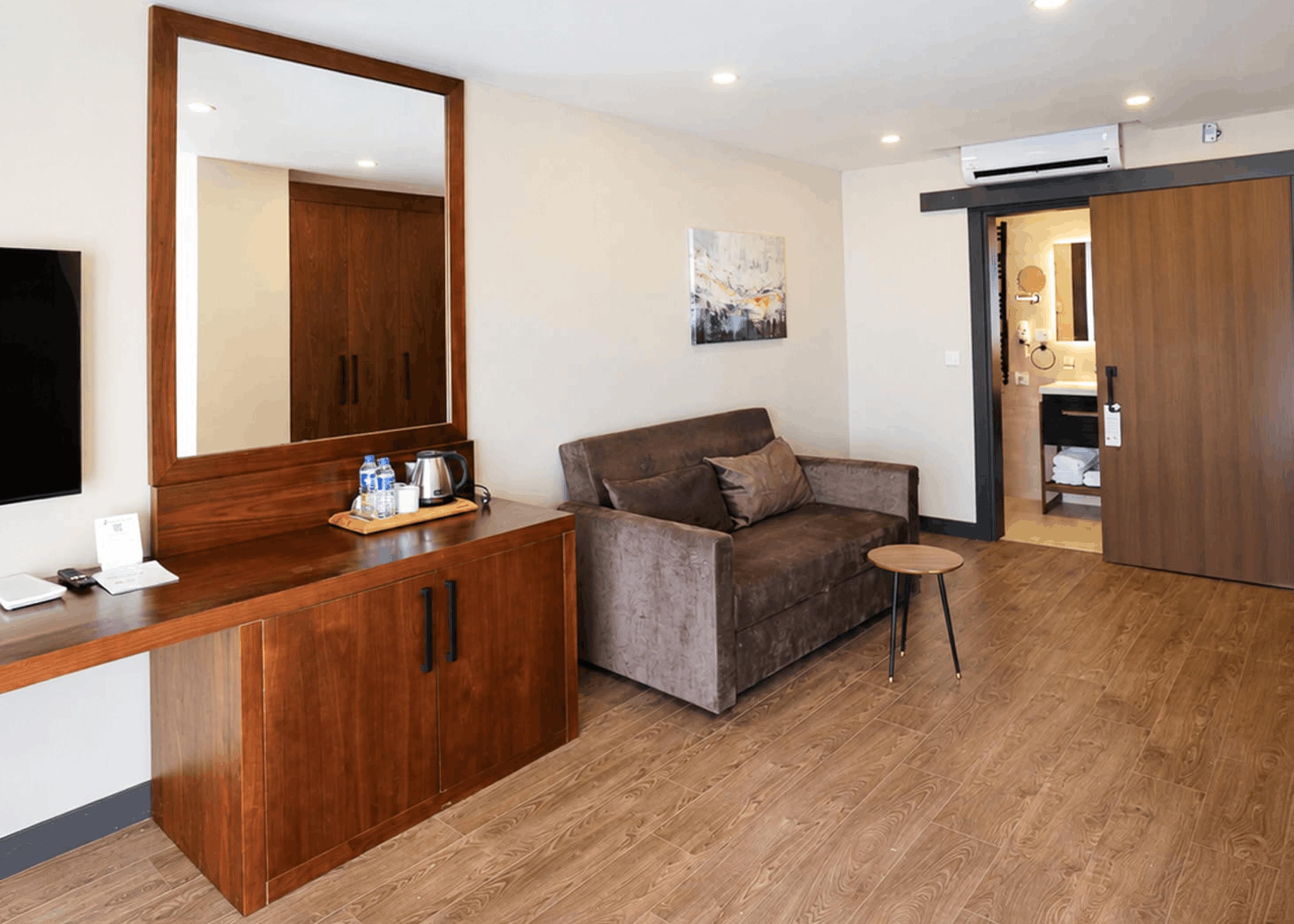 A modern room with a wooden desk, a sofa, a small round table, and a large mirror.
