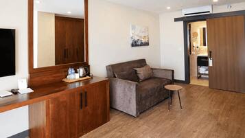 A modern room with a wooden desk, a sofa, a small round table, and a large mirror.