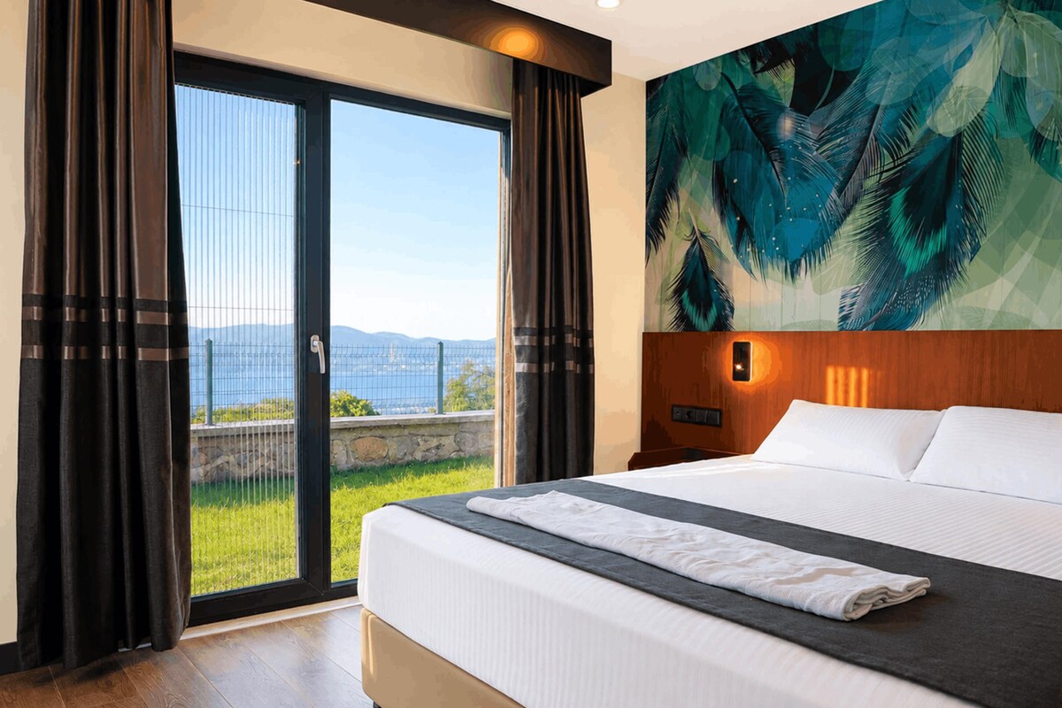 A hotel room with a large bed, a view of the sea, and a tropical mural on the wall.