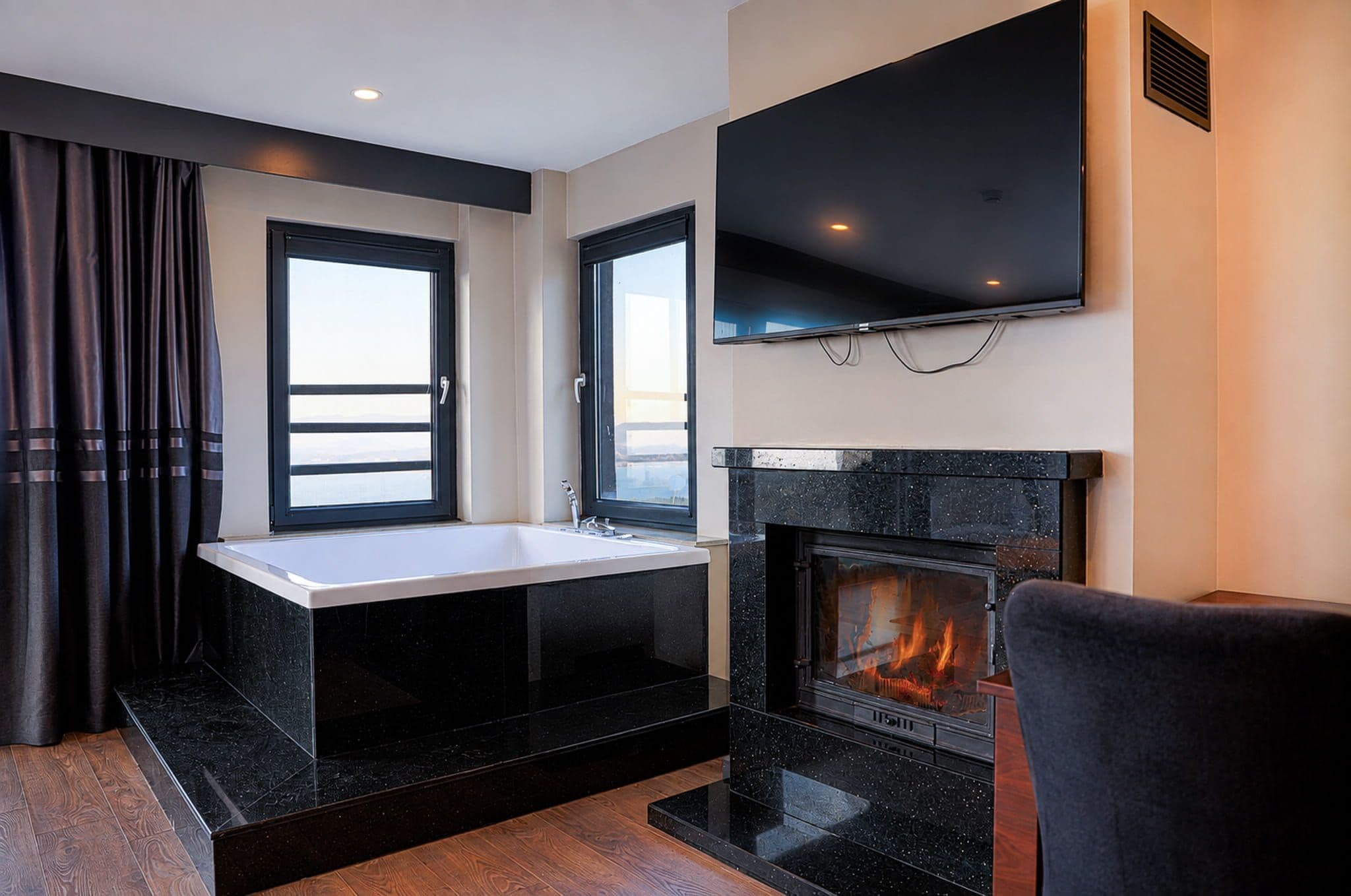 A modern living room with a fireplace, a flat-screen TV mounted above it, and a window with curtains.