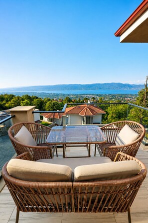 An outdoor patio with wicker furniture and a glass table, overlooking a scenic landscape with houses and a body of water. - Best Western Plus Sapanca (Sapanca)