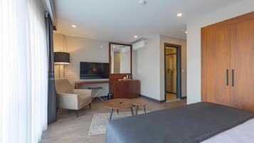 Una habitación de hotel moderna con cama, escritorio con silla, una mesita, lámpara y armario.