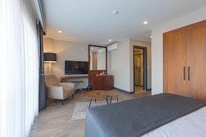 Ein modernes Hotelzimmer mit einem Bett, einem Schreibtisch mit Stuhl, einem kleinen Tisch, einer Lampe und einem Kleiderschrank.