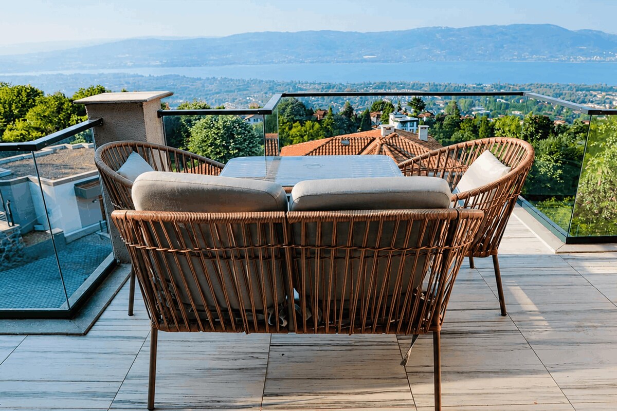 A terrace with wicker furniture and a glass balustrade overlooking a scenic landscape.