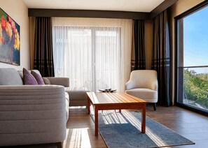A modern living room with a sofa, armchair, and coffee table, large windows with curtains, and a view of greenery outside. - Best Western Plus Sapanca (Sapanca)