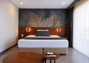 Une chambre d’hôtel moderne avec un grand lit, deux tables de chevet, une table basse ronde et un mur décoratif orné de motifs végétaux.