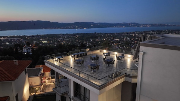 Eine Dachterrasse mit Tischen und Stühlen, mit Blick auf eine Stadtlandschaft und ein Gewässer.