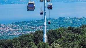 Un téléphérique composé de plusieurs cabines suspendues à des câbles, offrant une vue panoramique sur une ville côtière et la mer.