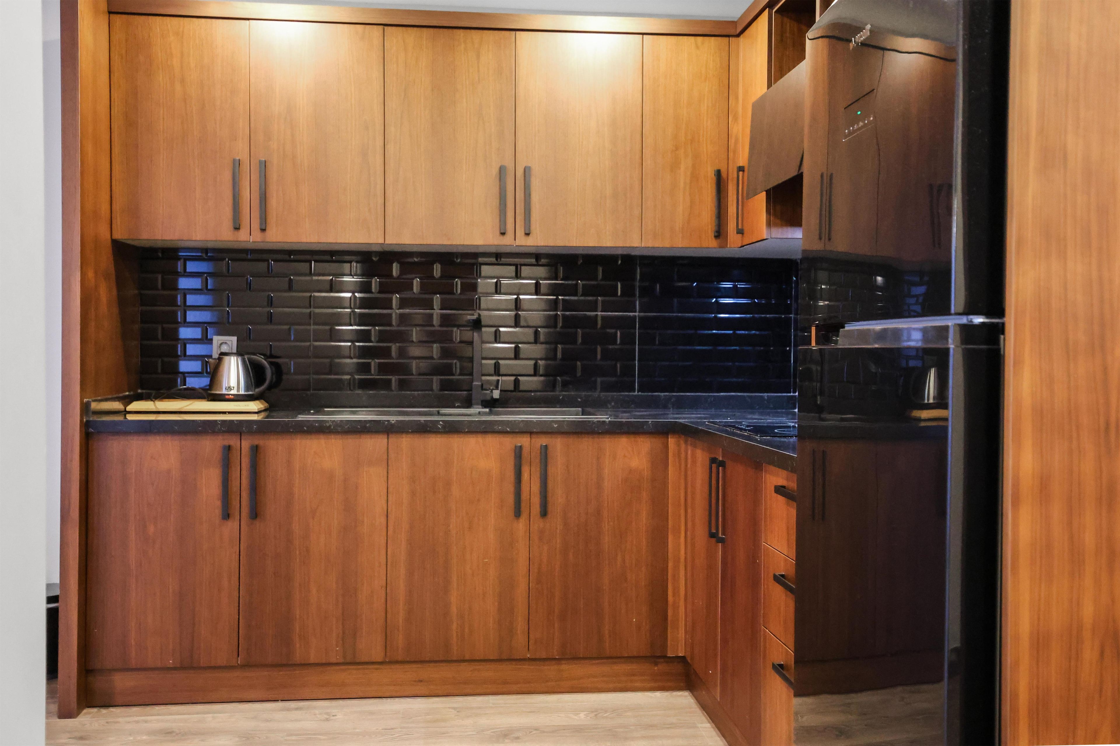 A kitchen with wooden cabinets, a black tiled backsplash, and stainless steel appliances.