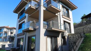 A modern multi-story residential building with balconies, large windows, and a stone retaining wall.