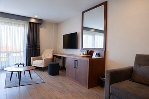 A modern hotel room with a sofa, a chair, a small table, a TV, a cabinet, and a large window with curtains. - Best Western Plus Sapanca (Sapanca)