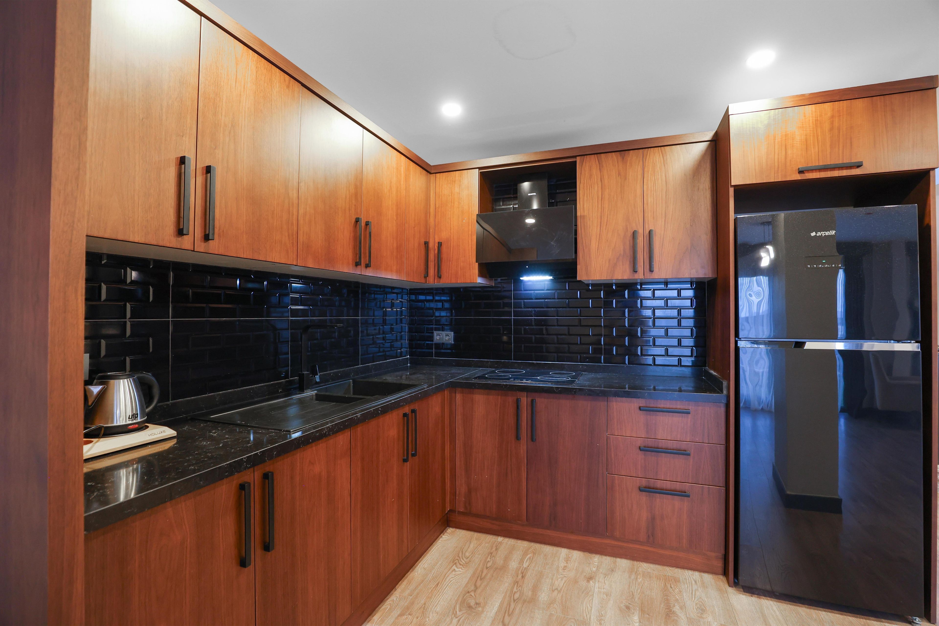 Una cocina moderna con armarios de madera, encimera negra y refrigerador de acero inoxidable.