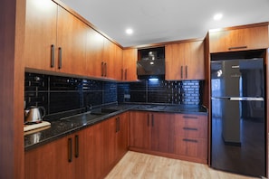 Eine moderne Küche mit Holzausstattung, einer schwarzen Arbeitsplatte und einem Edelstahlkühlschrank.