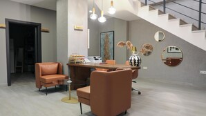 Un área de recepción moderna con un mostrador, dos sillones de cuero, una mesa de centro y una escalera.