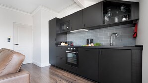 A modern kitchen with dark cabinetry, a stainless steel sink, and a built-in oven. - Lake Road Apartments (Bowness-on-Windermere)