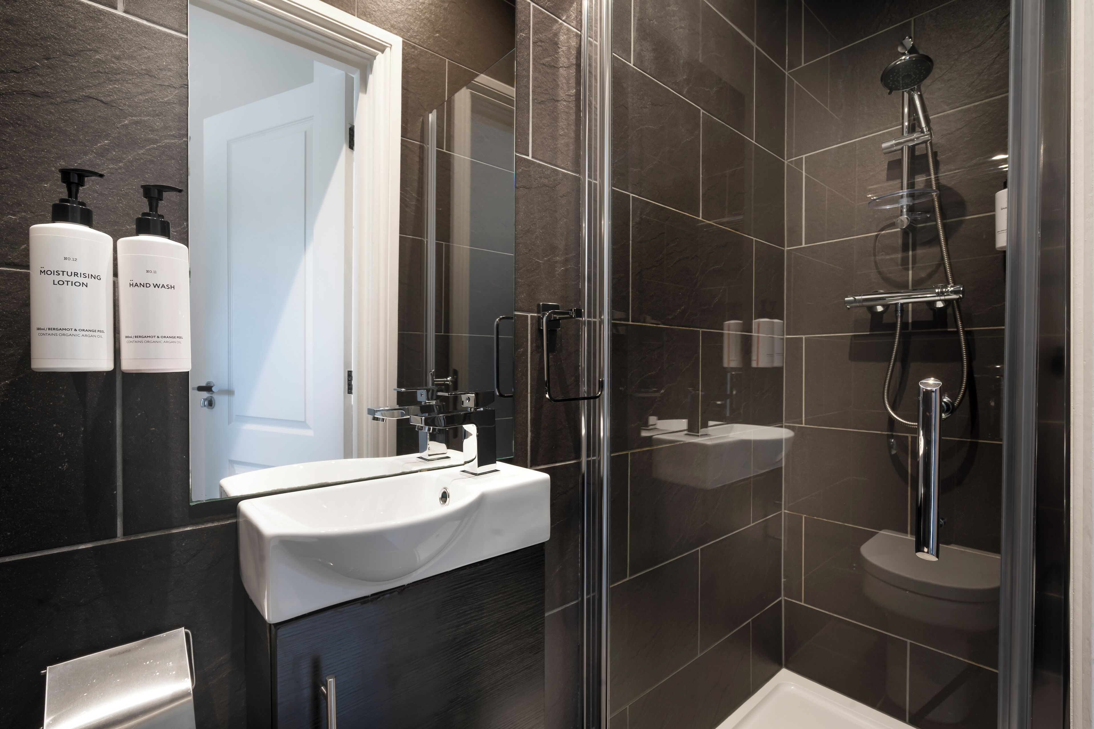 A modern bathroom with a glass-enclosed shower, a white sink, and a mirror above it.