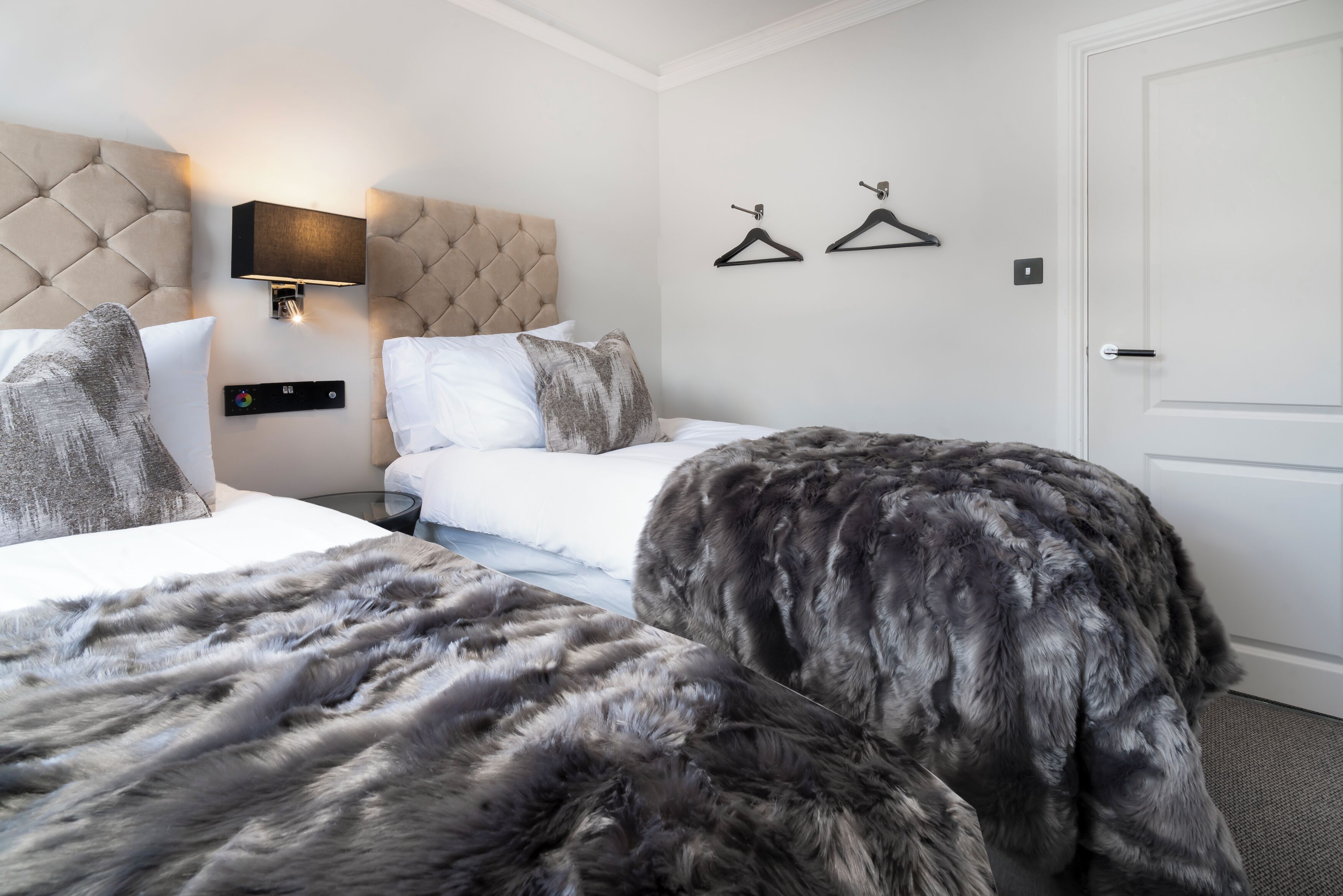 A hotel room with two beds, a tufted headboard, a wall-mounted TV, and two black hangers on the wall.