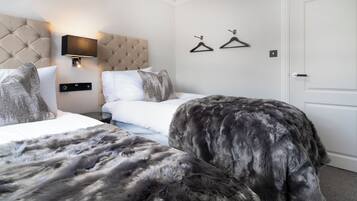 A hotel room with two beds, a tufted headboard, a wall-mounted TV, and two black hangers on the wall.