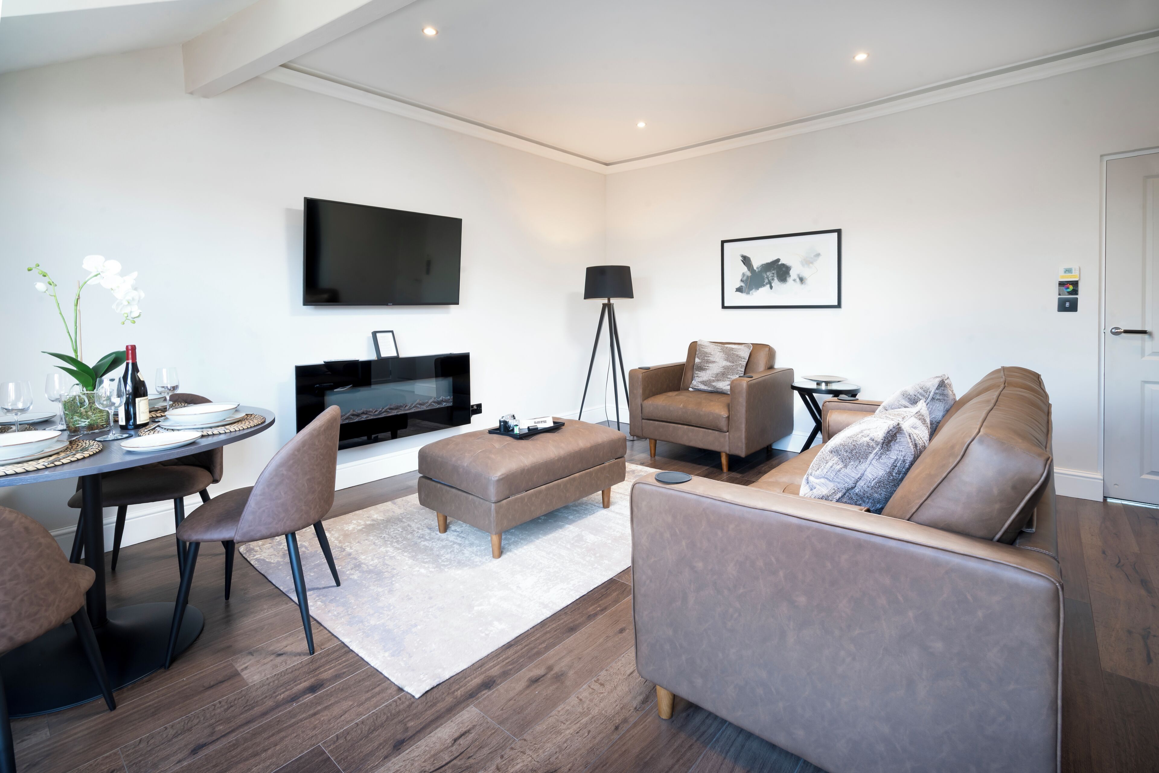 Un salon moderne doté d’un téléviseur à écran plat, d’un canapé, d’une table basse et d’un coin repas avec des chaises et une table dressée pour deux personnes.