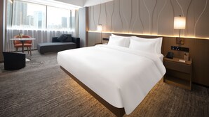 A modern hotel room with a large bed, a small table with a chair, a sofa, and a city view through the window. - Huayu Wanfu Hotel (Guangzhou)