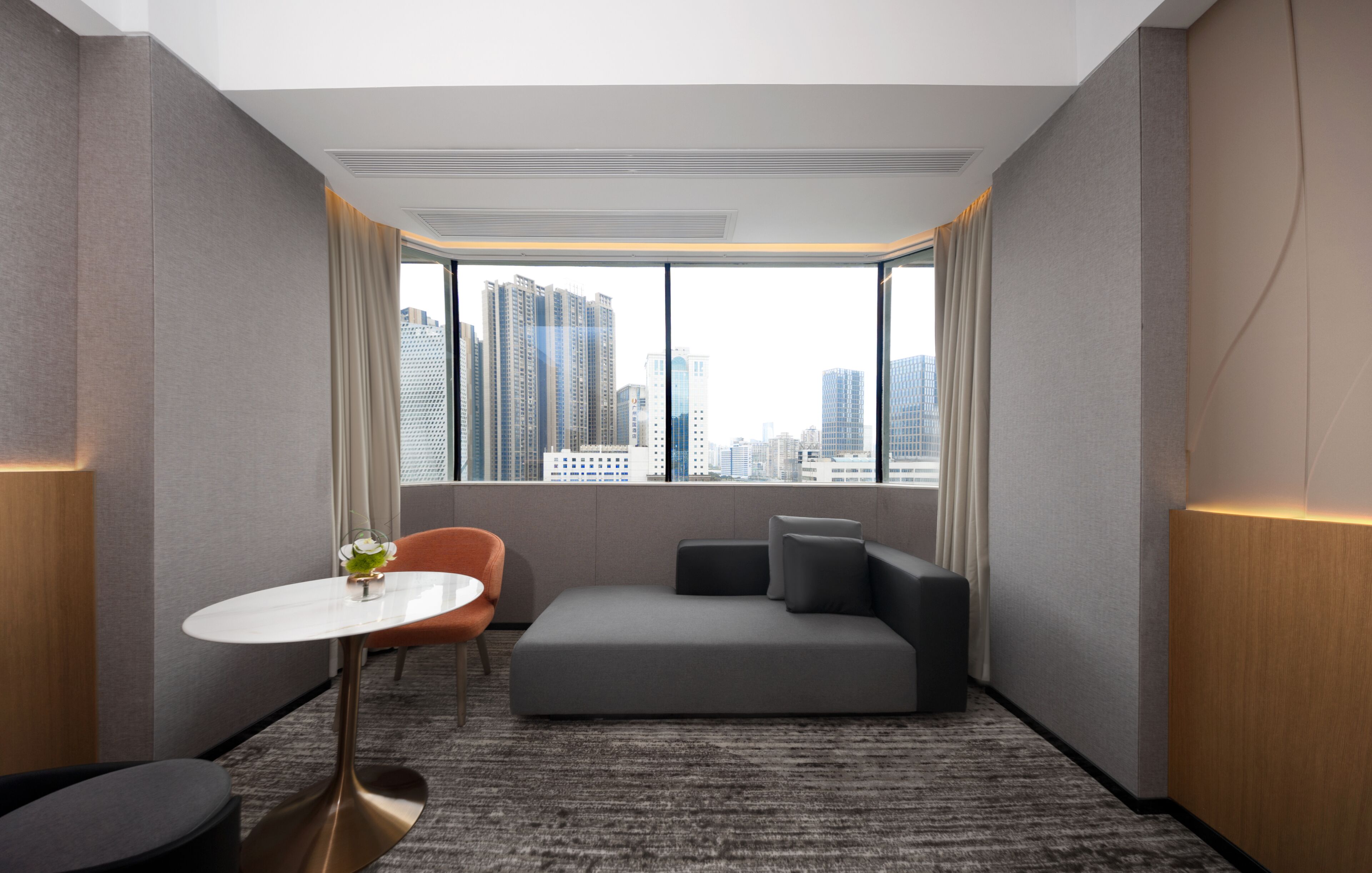 Habitación de hotel moderna con vista a la ciudad, una pequeña mesa redonda, un sofá y piso alfombrado.