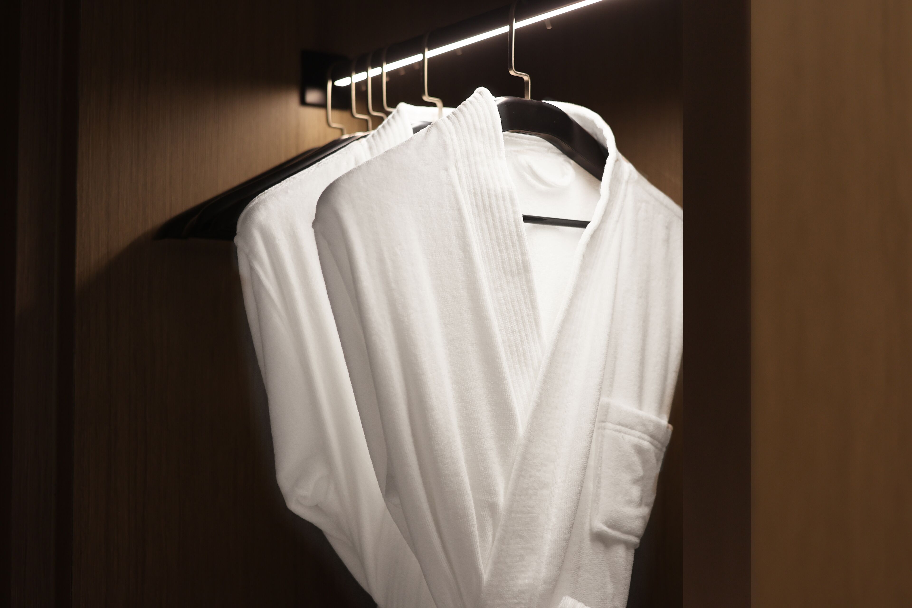 A white robe hanging on a black hanger in a dimly lit room with wooden walls.