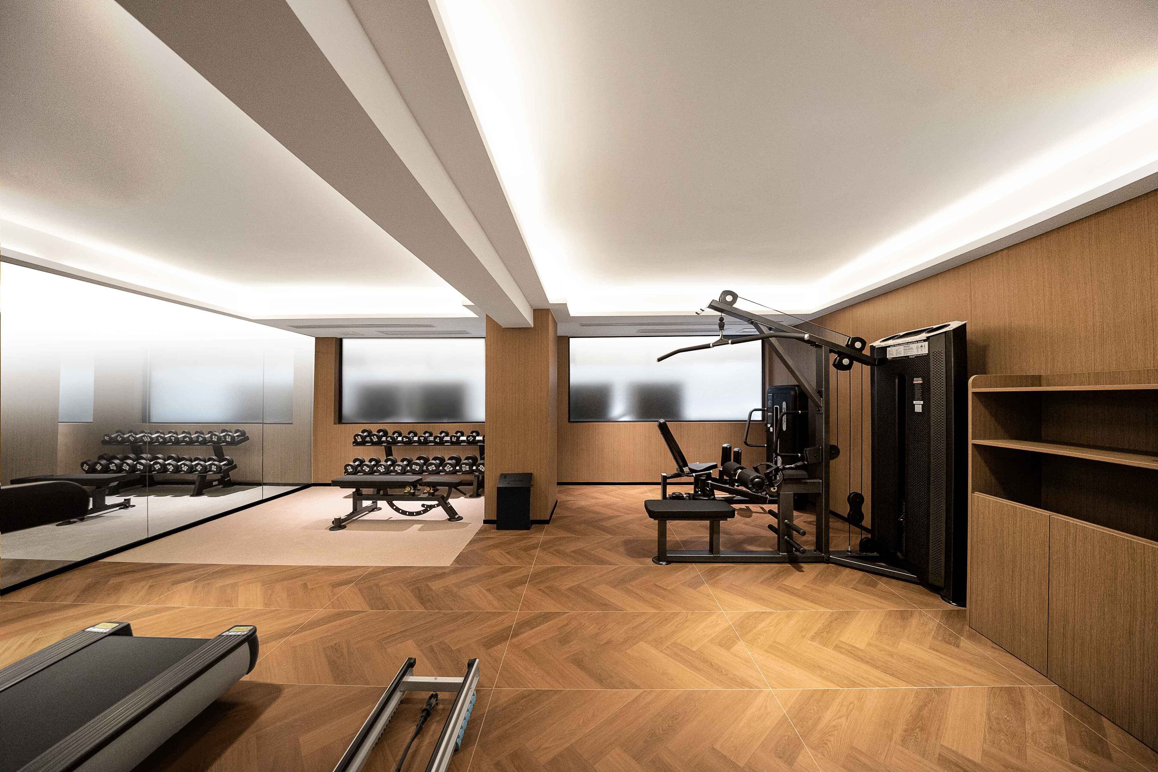 Ein modernes Fitnessstudio mit Trainingsgeräten, Spiegelwänden und einem Fischgrätparkettboden.