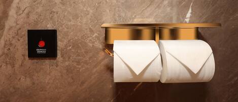 A marble wall with a gold flush mount toilet paper holder and a black emergency SOS button.