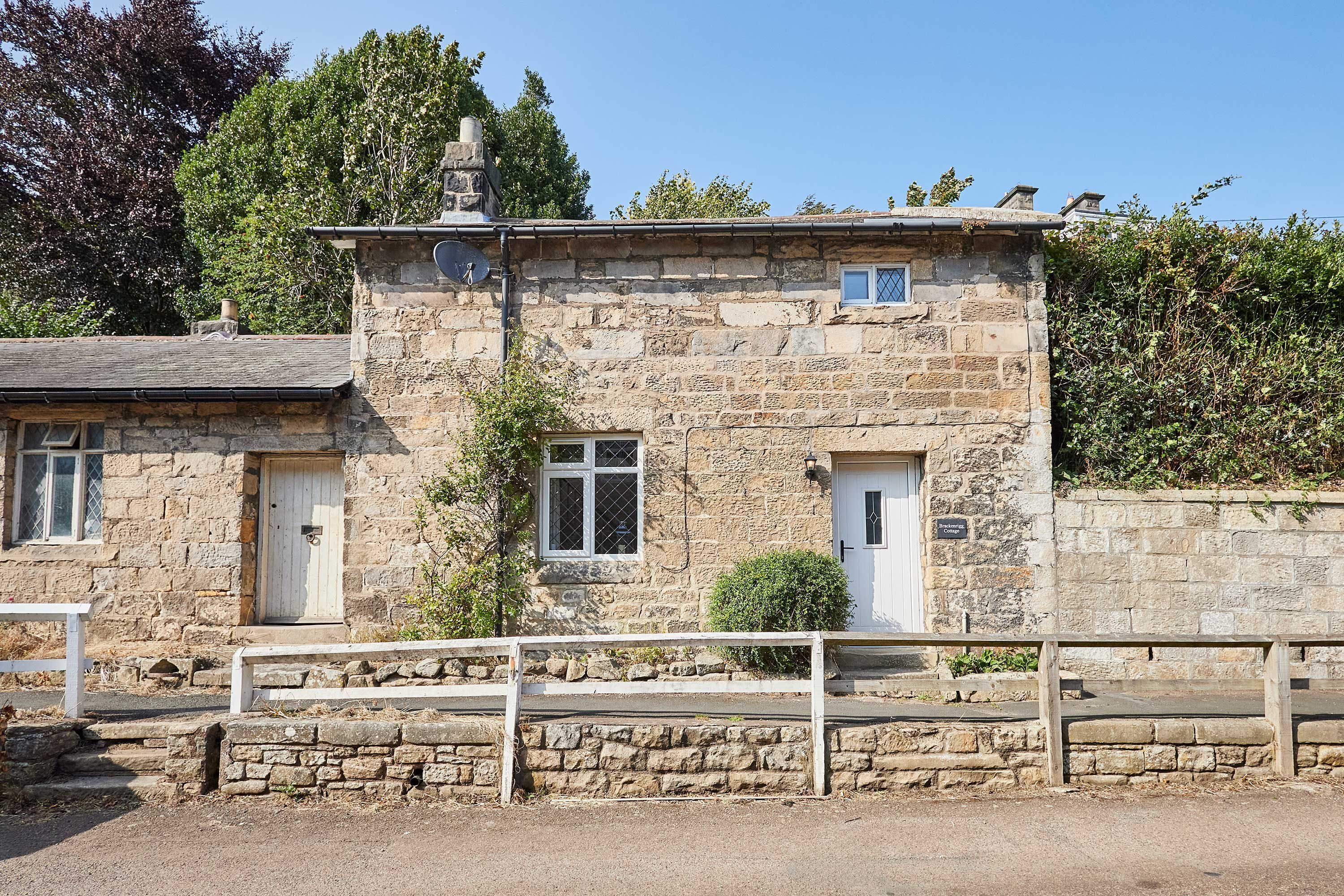 Un bâtiment en pierre à l’architecture traditionnelle, doté d’un petit porche et d’une clôture en bois à l’avant.