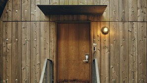 A wooden door with a metal handle and a keypad lock, a small light fixture above it, and a metal stairway leading up to the door. - SANU 2nd Home Nasu 1st (Nasu)