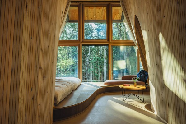 Una camera da letto con un letto a ferro di cavallo, un tavolino rotondo e una finestra vista foresta.