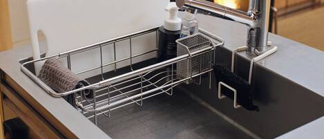 A kitchen sink with a dish rack, a soap dispenser, and a coffee maker.