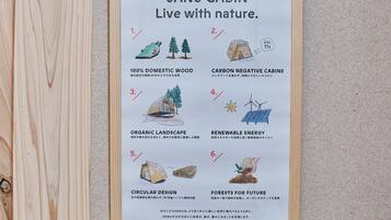 Póster enmarcado que detalla las características de la Cabaña Sanu, incluyendo madera 100% nacional, cabañas con huella de carbono negativa, paisaje orgánico, energía renovable, diseño circular y bosques para el futuro.