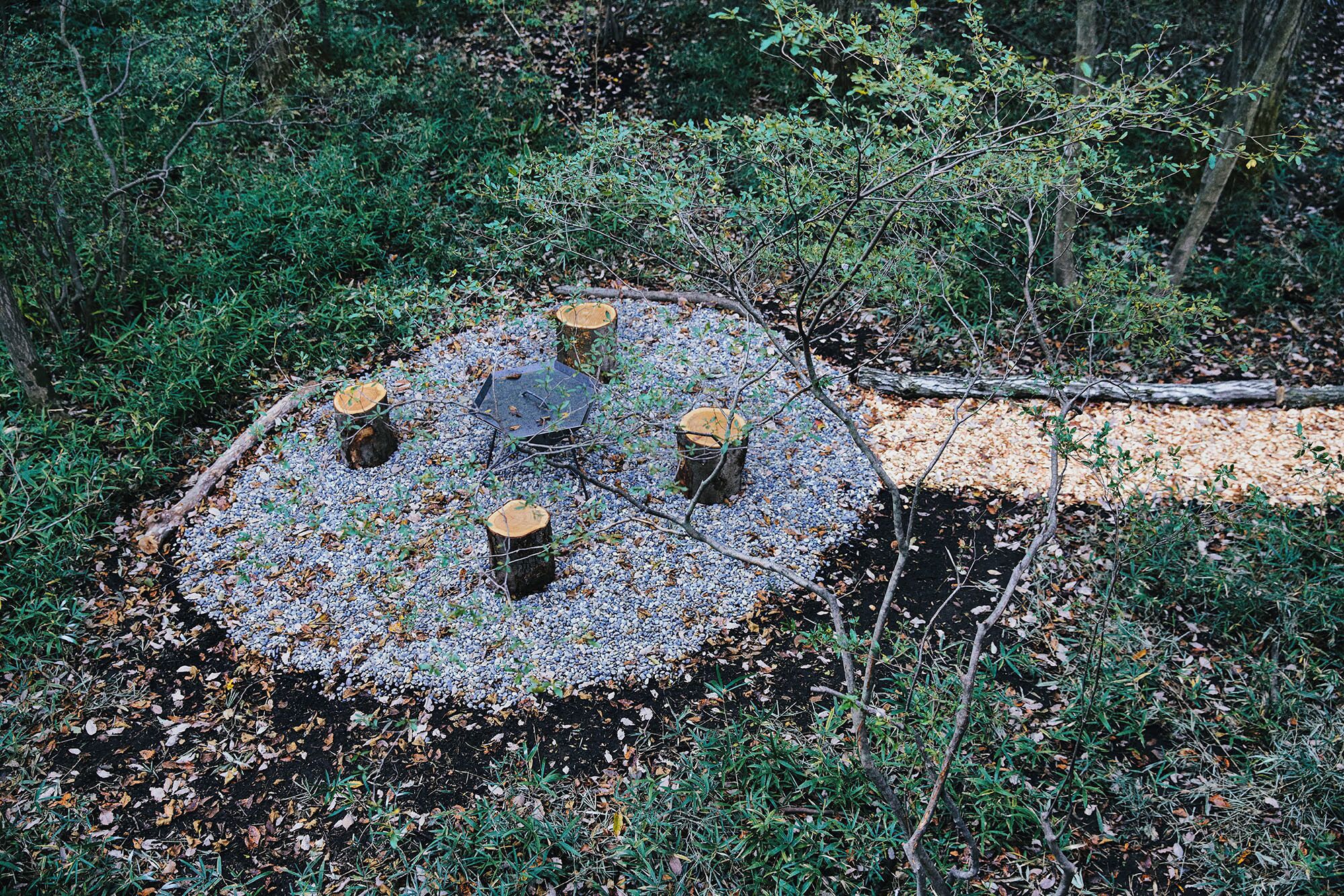 A circular outdoor seating area with a central table surrounded by six wooden stools.