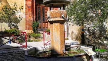 Une fontaine en pierre avec un bassin circulaire, entourée de murs de pierre et d’une rambarde en métal rouge.