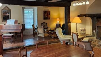 Un salon chaleureux avec une table à manger en bois, des fauteuils confortables, une cheminée et un piano.