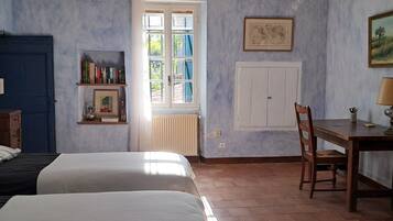 Une chambre avec deux lits, une table en bois, une chaise, un radiateur et une fenêtre avec des rideaux.