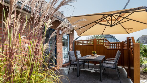 Een terras buiten met een tafel, stoelen, een houten schutting en een grote parasol.