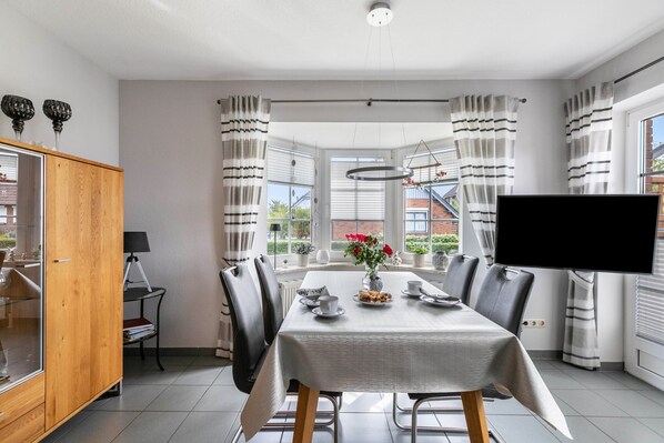 A dining area with a table set for four, a television, and a view of the outside.
